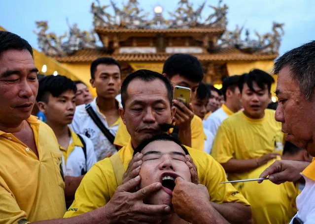 In this picture taken on October 5, 2016, an ethnic Malaysian-Chinese devotee (C) gets a spear skewered through his mouth on the fifth day of the annual Nine Emperor Gods festival at the Tow Boon Kong Nine Emperor Gods Temple in Butterworth. During the nine-day Taoist celebration, beginning on the eve of the ninth lunar month of the Chinese calendar, the festival welcomes the emperor gods that live in the stars under the reign of Thien Hou or the Queen of Heaven, who brings good fortune, longevity and good health. (Photo by Manan Vatsyayana/AFP Photo)
