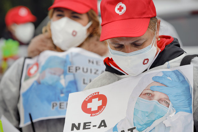 Medical workers, wearing masks for protection against the COVID-19 infection, protest outside the government headquarters demanding payment of the outstanding salaries and the opening of new positions in the national medical system to combat the current staff exhaustion, in Bucharest, Romania, Tuesday, November 3, 2020. Romania registered all time highs for new cases of COVID-19 infection on Tuesday. (Photo by Vadim Ghirda/AP Photo)
