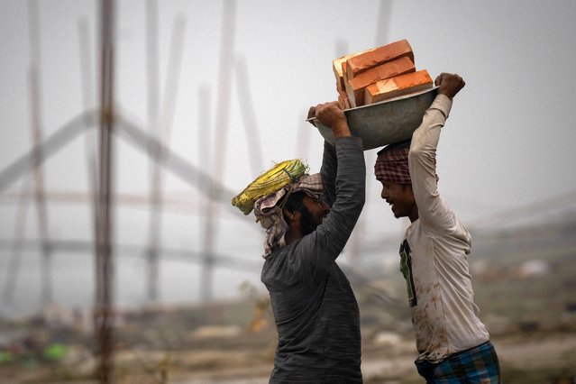 Laborers share a light moment as they carry bricks to be transported in a boat, in Guwahati, India, Tuesday, February 21, 2023. (Photo by Anupam Nath/AP Photo)