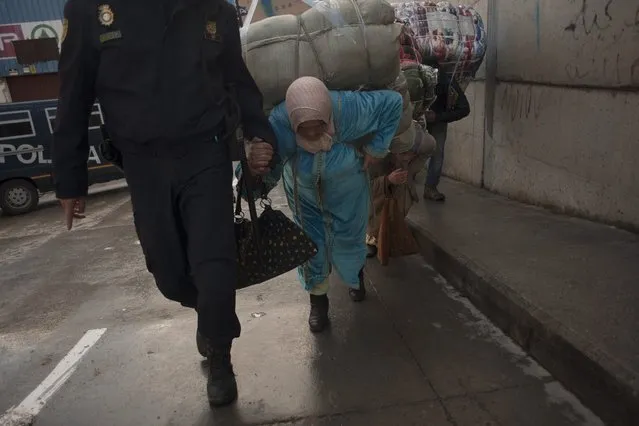 A policeman helps a women porter as she carries a bundle on their backs for transport across the El Tarajal boarder separating Morocco and Spain's North African enclave of Ceuta, in Ceuta on December 4, 2014. (Photo by Jorge Guerrero/AFP Photo)