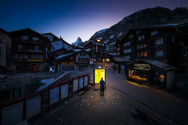 This photograph taken on March 18, 2020, shows a pedestrian looking at an illuminated map board in the empty streets of the Alpine resort of Zermatt, with the Matterhorn mountain amid the spread of the COVID-19 caused by the novel coronavirus. The Swiss government on March 16, 2020 declared a state of emergency lasting until April 19 in a bid to combat the coronavirus pandemic. All shops, restaurants, bars, entertainment and leisure facilities had to shut down, with the exception of grocery stores, pharmacies and health facilities. (Photo by Valentin Flauraud/AFP Photo)