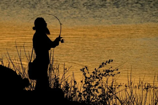 A man fishes at Shawnee Mission Lake at dusk Thursday, April 13, 2023, in Shawnee, Kan. (Photo by Charlie Riedel/AP Photo)