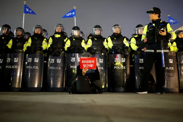 A woman holding up a placard that reads, "Step down Park Geun-hye" sits in front of riot police during a rally calling on embattled President Park to resign over a growing influence-peddling scandal in central Seoul, South Korea, November 5, 2016. (Photo by Kim Hong-Ji/Reuters)