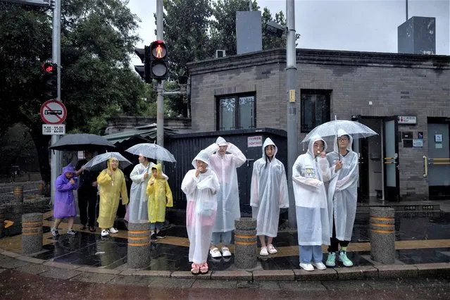 People wear raincoats in a tourist area during heavy rain in Beijing, China on July 30, 2023. (Photo by Thomas Peter/Reuters)