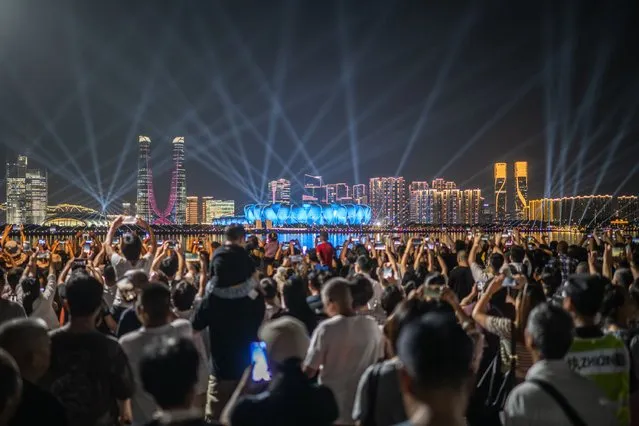 People gather at the promenade of Qiantang River to watch the light show of the Hangzhou Olympic Sports Centre Stadium (C), ahead of the 2022 Asian Games in Hangzhou in China's eastern Zhejiang province on September 19, 2023. (Photo by Philip Fong/AFP Photo)