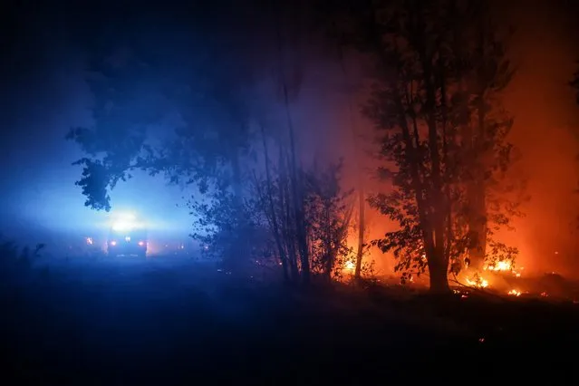 A firefighter vehicle drives on a road past flames at a wildfire near Belin-Beliet, southwestern France, overnight on August 11, 2022. French officials warned that flare-ups could cause a massive wildfire to further spread in the country's parched southwest, where fresh blazes have already blackened swathes of land this week. Prime Minister is expected to meet with authorities battling the Landiras blaze south of Bordeaux, and further reinforcements are expected for the 1,100 firefighters on site, the prefecture of the Gironde department said. (Photo by Thibaud Moritz/AFP Photo)