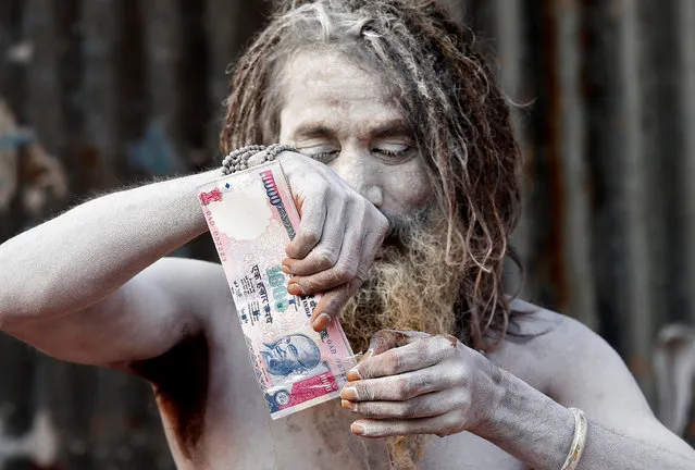 A Sadhu or Hindu holy man with his face covered with ash puts a wallet decorated with a print of the scrapped Indian 1000-rupee note, which he received as a gift from a devotee, inside a plastic cover at a makeshift shelter in Kolkata, India, January 5, 2017. (Photo by Rupak De Chowdhuri/Reuters)