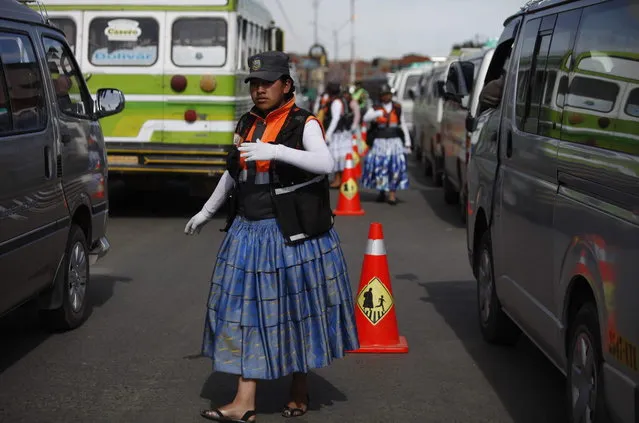 In this December 3, 2013 photo, an Aymara woman cops directs traffic on the streets of El Alto, Bolivia. The women wear the bright petticoats and shawls of indigenous women in the Andes, called cholitas in Bolivian slang, the main difference being that instead of bowler hats they wear khaki green police-style caps. Some don fluorescent traffic vests. (Photo by Juan Karita/AP Photo)