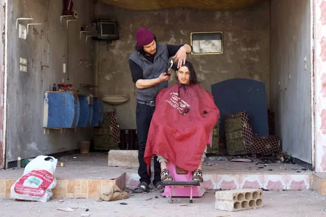 A barber cuts the hair of a customer outside his damaged salon in the rebel held al-Ghariyah al-Gharbiyah town, in Deraa province, Syria February 28, 2016. (Photo by Alaa Al-Faqir/Reuters)