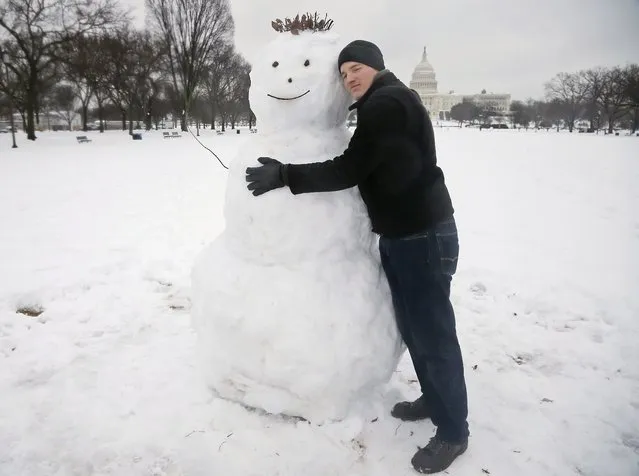 Larry Gard from Chicago hugs a snowman he just built on the National Mall in Washington, Thursday, February 13, 2014. After pummeling wide swaths of the South, a winter storm dumped nearly a foot of snow in Washington as it marched Northeast and threatened more power outages, traffic headaches and widespread closures for millions of residents. (Photo by Charles Dharapak/AP Photo)