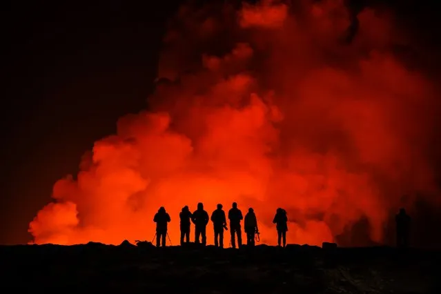 People look at the volcano erupting, north of GrindavÌk, Iceland, Thursday, February 8, 2024. Icelandís Meteorological Office says a volcano is erupting in the southwestern part of the country, north of a nearby settlement. The eruption of the Sylingarfell volcano began at 6 a.m. local time on Thursday, soon after an intense burst of seismic activity. (Photo by Marco Di Marco/AP Photo)