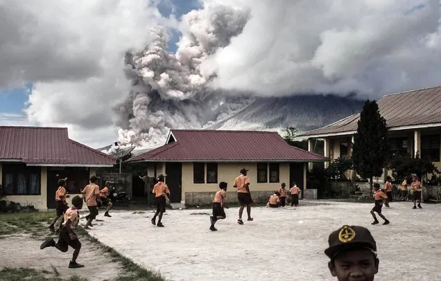 Elementary school children play outside of their classrooms as mount Sinabung volcano spews thick volcanic ash as seen from Karo, North Sumatra province, on February 10, 2017. Many residents in the area have been forced to relocate to other villages of Northern Sumatra at a safer distance from mount Sinabung volcano, one of the most active in Indonesia. (Photo by AFP Photo/Stringer)