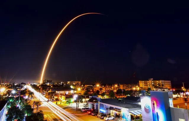 In this image taken with a long exposure, a SpaceX Falcon 9 rocket carrying the 32nd batch of Starlink internet satellites arches over the skyline of Cocoa Beach, Fla., Thursday evening, December 2, 2021, after blasting off from Cape Canaveral. (Photo by Malcolm Denemark/Florida Today via AP Photo)