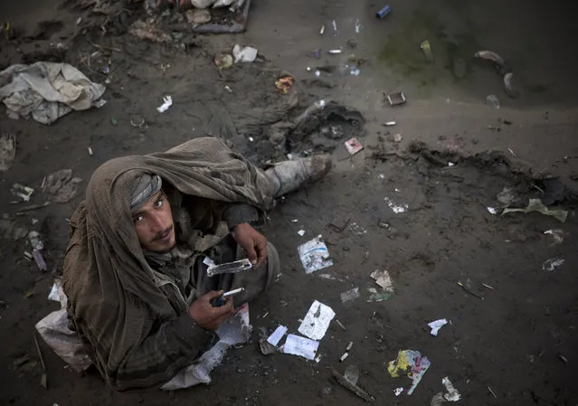 In this Saturday, November 9, 2013 photo, an Afghan drug addict smokes opium in a foul smelling river bed in the center of Kabul. More than 1 million Afghans are addicts, living in squalor in its cities, sleeping on the street, in garbage-filled dried river beds reeking of human waste. (Photo by Anja Niedringhaus/AP Photo)