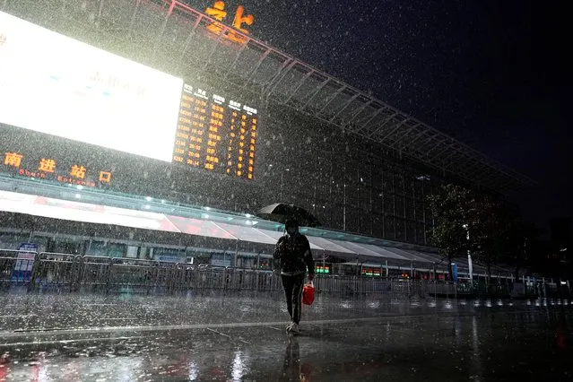 A man wearing a face mask walks in the rain past an information board displaying trains that have stopped operating, outside Shanghai Railway Station following the coronavirus disease (COVID-19) outbreak in Shanghai, China on March 21, 2022. (Photo by Aly Song/Reuters)