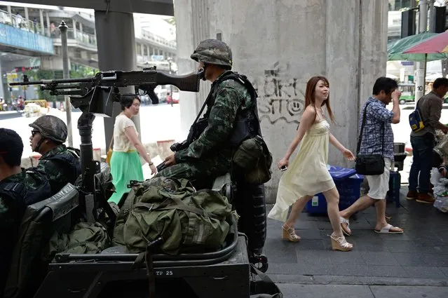 People walk past Thai army soldiers sitting in a jeep mounted with a machine gun as they secure a main intersection in Bangkok on May 20, 2014. Thailand's army declared martial law across the deeply divided kingdom on May 20 to restore order after months of deadly anti-government protests, deploying armed troops in the capital but insisting the move was “not a coup”. (Photo by Christophe Archambault/AFP Photo)
