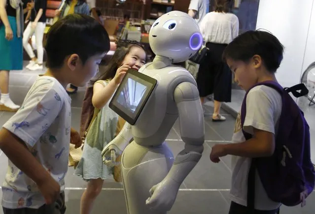 In this photo taken Sunday, July 12, 2015, children surround SoftBank Corp.'s new companion robot Pepper at a store in Tokyo. Pepper, the 121-centimeter (four-foot) tall white machine-on-wheels, offers ardent attention, cool dance moves, and small talk. Pepper has cameras, lasers and infrared in its hairless head so it can detect human faces. (Photo by Shizuo Kambayashi/AP Photo)