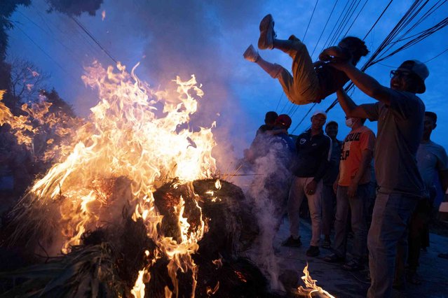 A man swings his son over a burning effigy of demon Ghantakarna which represents the demolition of evil during the Ghantakarna festival in Bhaktapur, Nepal, Friday, August 2, 2024. (Photo by Niranjan Shrestha/AP Photo)