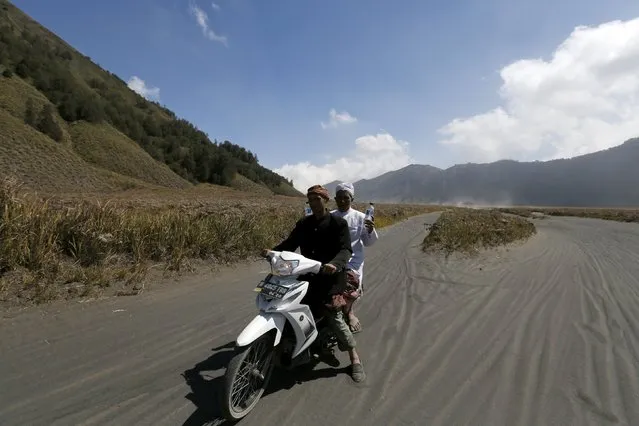 Hindu villagers ride a motorcycle as they carry holy water they collected for prayers ahead of the annual Kasada festival at Mount Bromo in Indonesia's East Java province, July 30, 2015. The Kasada festival will be held on August 1, when the worshippers throw offerings such as livestock and other crops into the volcanic crater of Mount Bromo to give thanks to the Hindu gods for ensuring their safety and prosperity. (Photo by Reuters/Beawiharta)