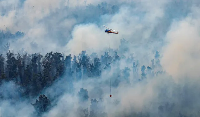 This handout photo taken on December 29, 2019 and received on December 30 from Victoria's Department of Environment, Land, Water and Planning (DELWP) shows a helicopter dumping water on a fire in Victoria's East Gippsland region. Tourists and firefighters were forced to flee vast fires burning in southeastern Australia on December 30, as a heatwave rekindled devastating bush blazes across the country. (Photo by Handout/Department of Environment, Land, Water and Planning/AFP Photo)