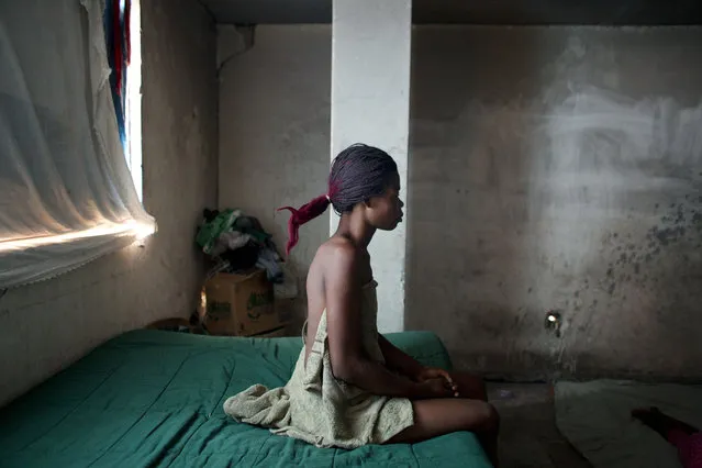 In this June 29, 2015 photo, hairdresser Loavia Bienaime, 30, sits on her bed as she prepares to begin her day in the room her family occupies in an government office building that was damaged in the 2010 earthquake in Port-au-Prince, Haiti. Bienaime's husband, Jimmy Bellefleur, used his skill as an electrician to connect the abandoned building to the power grid, and has repaired broken televisions, fans, and a blender for the family to use. (Photo by Rebecca Blackwell/AP Photo)