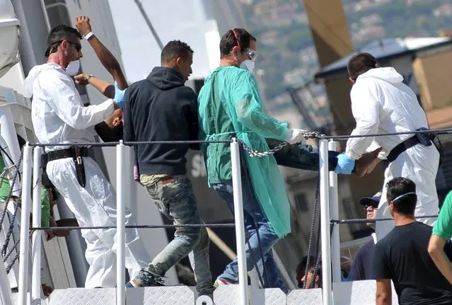 A migrant is helped to disembark from Italian Coast Guard vessel Diciotti in the Sicilian harbour of Palermo, Italy, August 20, 2015. (Photo by Guglielmo Mangiapane/Reuters)