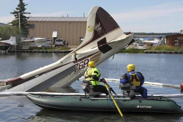 Two men in a raft row to the partially submerged wreckage of a plane that crashed at the Lake Hood seaplane base in Anchorage, Alaska, Tuesday, July 26, 2022. Authorities say all six people on board the aircraft were injured, two seriously. (Photo by Mark Thiessen/AP Photo)