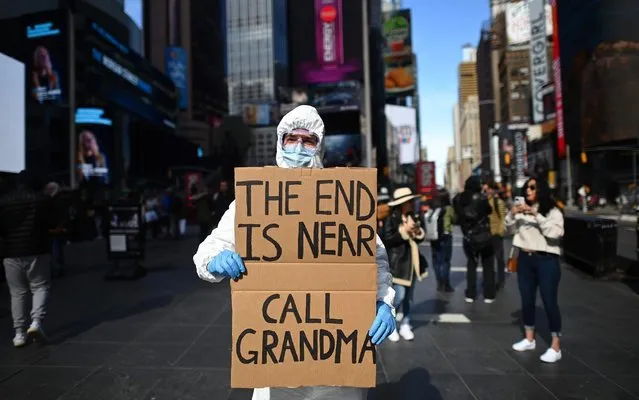 A man wearing a hazmat suit and a mask holds a sign reading “The end is near – call grandma” at Times Square on March 14, 2020 in New York City. The World Health Organization said March 13, 2020 it was not yet possible to say when the COVID-19 pandemic, which has killed more than 5,000 people worldwide, will peak. “It's impossible for us to say when this will peak globally”, Maria Van Kerkhove, who heads the WHO's emerging diseases unit, told a virtual press conference, adding that “we hope that it is sooner rather than later”. (Photo by Johannes Eisele/AFP Photo)