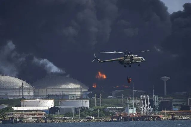 A helicopter carrying water flies over the Matanzas Supertanker Base, as firefighters try to quell the blaze which began during a thunderstorm the night before, in Matazanas, Cuba, Saturday, August 6, 2022. Cuban authorities say lightning struck a crude oil storage tank at the base, causing a fire that led to four explosions which injured more than 50 people. (Photo by Ramon Espinosa/AP Photo)