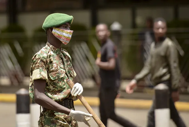 A member of the Kenya Youth Service wears a cloth face mask as he keeps members of the public at a distance as volunteers disinfect a road in an attempt to curb the spread of the new coronavirus, in downtown Nairobi, Kenya Friday, April 3, 2020. (Photo by John Muchucha/AP Photo)