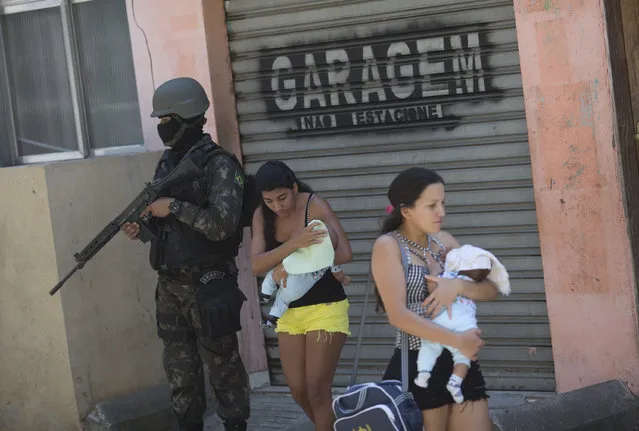 Women cradle their babies as they walk past a soldier during an operation at the Rocinha slum, in Rio de Janeiro, Brazil, Tuesday, October 10, 2017. More than 1,000 Brazilian police and soldiers are searching Rio's largest slum for weapons and ammunition amid a crackdown on drug gangs. In recent weeks, a series of intense shootouts led Brazilian authorities to ask the military for help patrolling the perimeter of Rocinha. (Photo by Silvia Izquierdo/AP Photo)