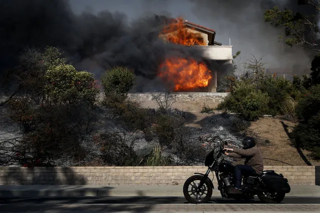 A man rides his bike past a home consumed by a wildfire Tuesday, December 5, 2017, in Ventura, Calif. (Photo by Jae C. Hong/AP Photo)
