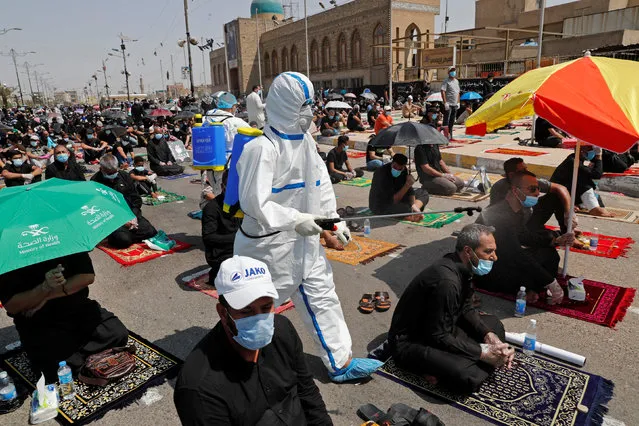 A volunteer wearing a protective suit sprinkles disinfectant as supporters of Iraqi Shi'ite cleric Moqtada al-Sadr attend Friday prayers for the first time in months since the coronavirus disease (COVID-19) restrictions were imposed, in Baghdad's Sadr City, Iraq on September 11, 2020. (Photo by Thaier Al-Sudani/Reuters)