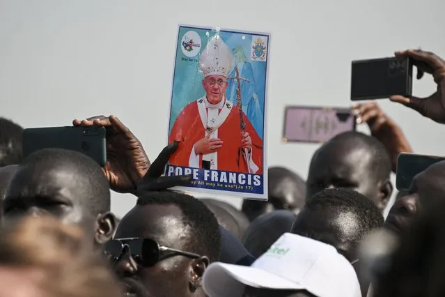 A man holds a picture of Pope Francis as a crowd gathers to welcome him upon his arrival at the Juba International Airport in Juba, South Sudan, on February 3, 2023. Pope Francis arrived on a three-day visit to South Sudan on February 3, 2023 to promote peace and reconciliation in the world's youngest country, riven by the scars of civil war and extreme poverty. (Photo by Tiziana Fabi/AFP Photo)
