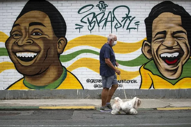 A man walks his dog past a mural of Brazilian soccer stars Pele, left, and Garrincha in Rio de Janerio, Brazil, Friday, December 30, 2022. Edson Arantes do Nascimento, known to the world as Pele, died in Sao Paulo Thursday at the age of 82. (Photo by Bruna Prado/AP Photo)