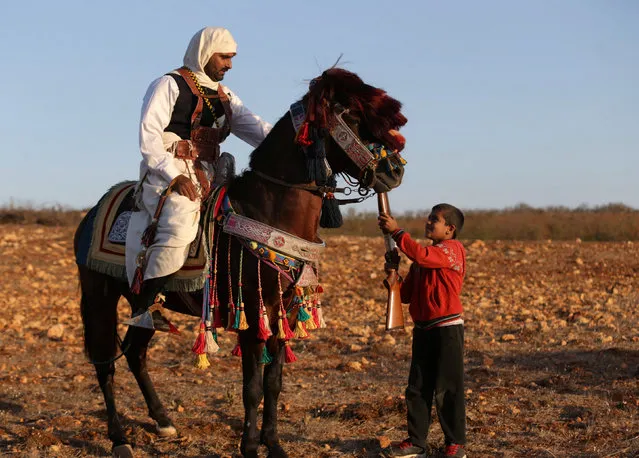 A boy hands a weapon to his father, dressed in a traditional costume as he rides a horse during a wedding parade in Shahhat, Libya October 1, 2016. (Photo by Esam Omran Al-Fetori/Reuters)