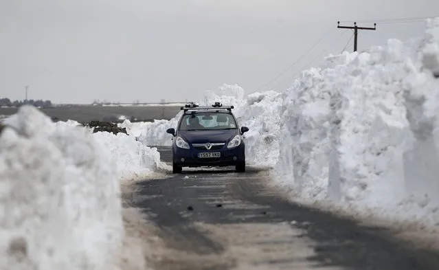 A car makes its way through a wall of snow piled up along a road in the Briercliffe area of Burnley, on March 25, 2013. A weekend of freezing cold weather and snow is continuing to cause disruption today, with thousands of homes across the UK without power and many roads still impassable. (Photo by Dave Thompson/PA Wire)