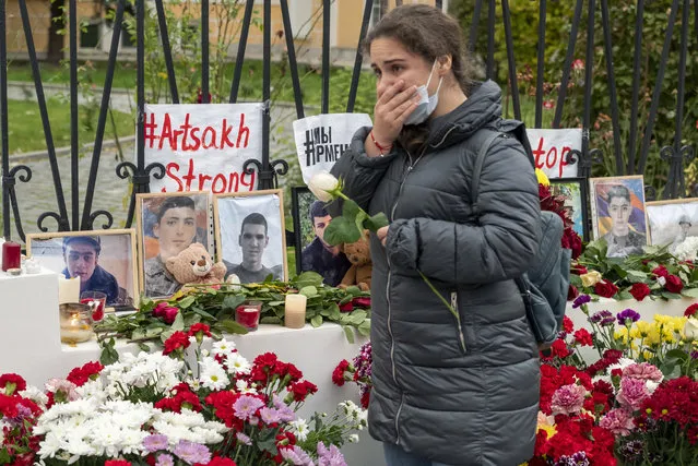 A woman reacts as she lays a flower at a symbolic memorial of victims of the military conflict in the separatist region of Nagorno-Karabakh at the Armenian Embassy in Moscow, Russia, Saturday, October 17, 2020. Nagorno-Karabakh lies within Azerbaijan but has been under the control of ethnic Armenian forces backed by Armenia since a war there ended in 1994. The latest outburst of fighting began on Sept. 27 and has involved heavy artillery, rockets and drones, killing hundreds and marking the largest escalation of hostilities between the South Caucasus neighbors in more than a quarter-century. (Photo by Mikhail Kirakosyan/AP Photo)
