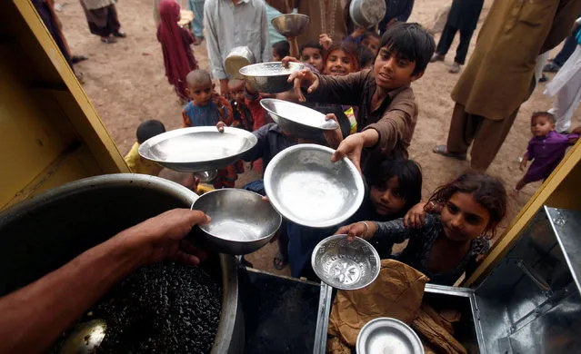 Children hold their bowls as they wait in line for a charity food handout in Peshawar, Pakistan March 13, 2018. (Photo by Fayaz  Aziz/Reuters)