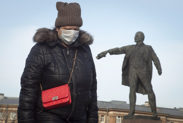 A woman wearing face mask walks past a statue of Soviet Union founder Vladimir Lenin in St.Petersburg, Russia, Friday, March 27, 2020. (Photo by Dmitri Lovetsky/AP Photo)