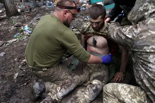 Military paramedics treat an Ukrainian injured serviceman on a street in the frontline city of Bakhmut, Donetsk region on April 23, 2023, amid the Russian invasion of Ukraine. (Photo by Anatolii Stepanov/AFP Photo)