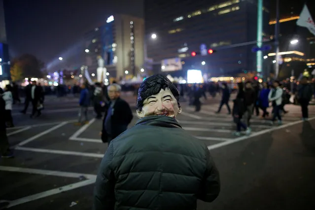 A man wearing a mask depicting South Korean President Park Geun-hye watches South Koreans take part in a rally calling on embattled Park to resign over a growing influence-peddling scandal in central Seoul, South Korea, November 5, 2016. (Photo by Kim Hong-Ji/Reuters)