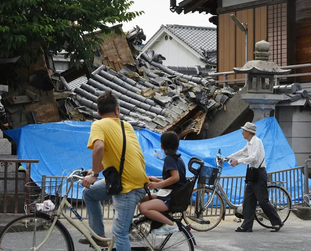 People pause to look at a collapsed house following an earthquake in Ibaraki City, north of Osaka prefecture on June 18, 2018. At least two people, including a child, were killed on June 18, after a strong quake rocked the second city of Osaka during the morning rush hour, Japan's government said. (Photo by AFP Photo/JIJI Press)