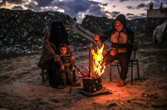 A couple and their son warm themselves by a fire near their makeshift house during cold weather in the south of the Khan Younis Refugee Camp in the Gaza Strip, 19 February 2021. (Photo by Mohammed Saber/EPA/EFE)