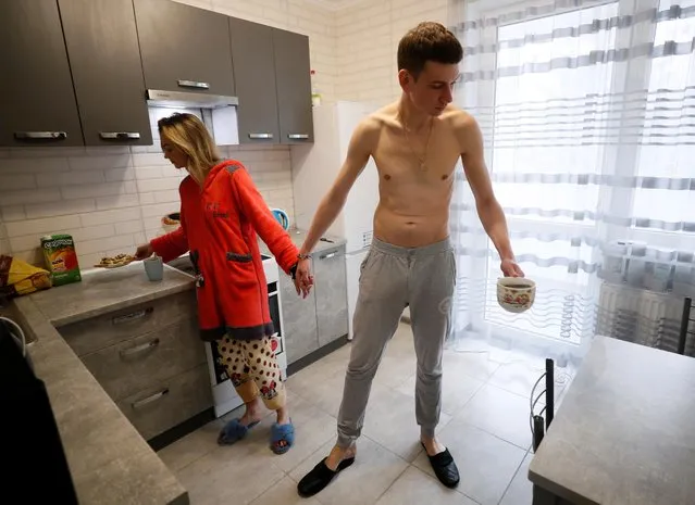Alexandr Kudlay, 33, and Viktoria Pustovitova, 28, make breakfast in their apartment in Kharkiv, Ukraine on March 5, 2021. Pustovitova refused his idea at first, hanging up the phone on him the first time he suggested it, but eventually changed her mind. For nearly a month now, neither has had any personal space and they do everything together, from grocery shopping to cigarette breaks. “I decided it will be an interesting experience for me, that it will bring into my life new bright emotions which I did not experience before”, Pustovitova said. “I love him, so I came to a decision to do it”. (Photo by Gleb Garanich/Reuters)