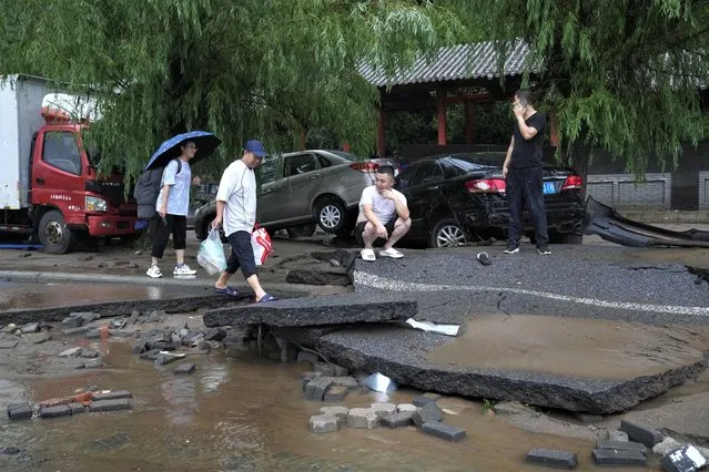 People walk along a damaged road and vehicles swept by flood water in the Mentougou District as continuous rainfall triggers alerts in Beijing, Monday, July 31, 2023. (Photo by Andy Wong/AP Photo)