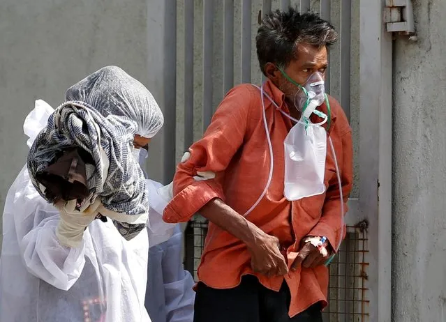 A patient with breathing problem is helped to walk towards an ambulance as he is being shifted to a hospital, amidst the spread of the coronavirus disease (COVID-19) in Ahmedabad, India, April 14, 2021. (Photo by Amit Dave/Reuters)