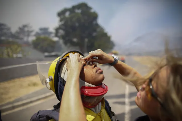A paramedic flushes the eyes of a fire fighter with saline solution to clear them of ash and debris in the midst of a blaze in Ocean View, Cape Town, South Africa, 11 January 2016. (Photo by Nic Bothma/EPA)