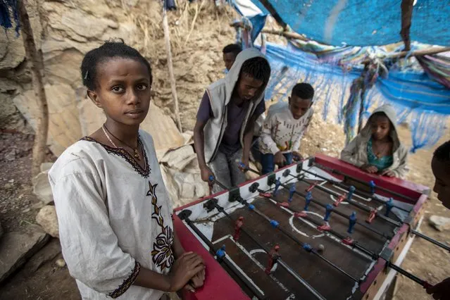 A girl watches while boys and young men play table football on the street, as Ethiopian Orthodox Christians celebrate Easter Sunday, in Gondar, in the Amhara region of Ethiopia Sunday, May 2, 2021. (Photo by Ben Curtis/AP Photo)