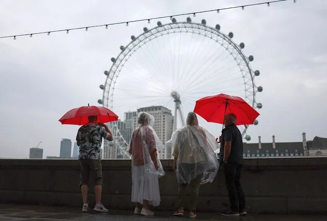 Pedestrians shelter from the rain beneath umbrellas while looking at the London landmark, the London Eye, from Embankment by the River Thames, in central London, on August 18, 2023 on a gloomy summer's day. (Photo by Henry Nicholls/AFP Photo)